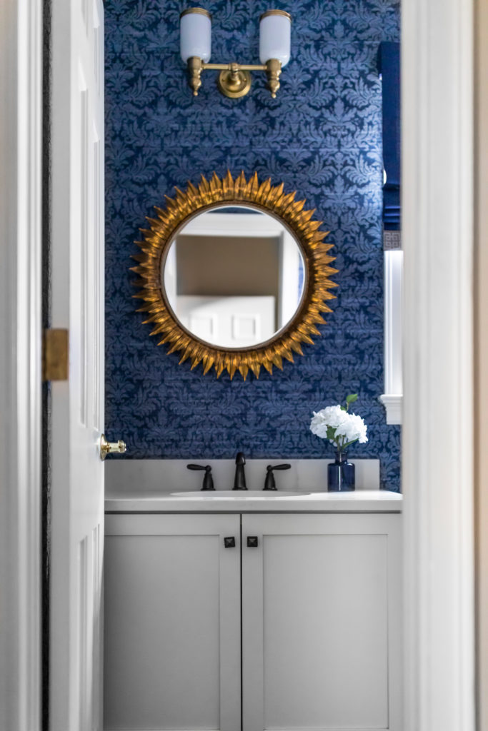 Dark blue damask wallpaper, antiqued gold leaf round mirror, and brass vanity sconce Lindsey Putzier Design Studio