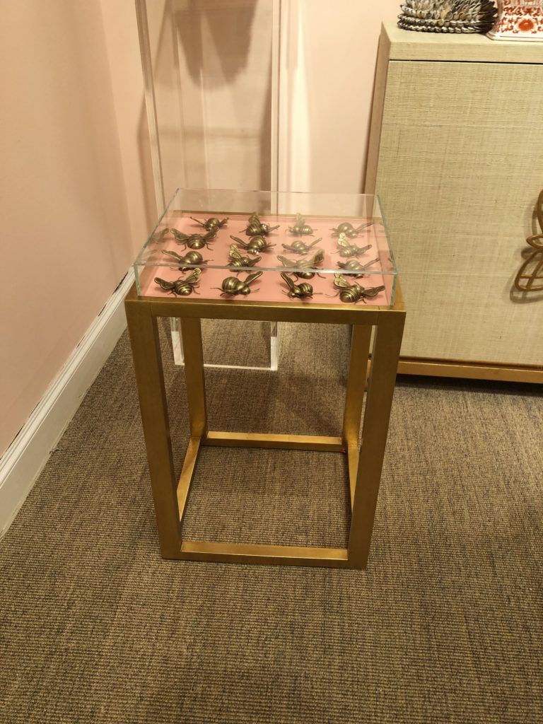 Gold based statement table featuring a case with a pink table top with golden bee sculptures within the case Lindsey Putzier Design Studio