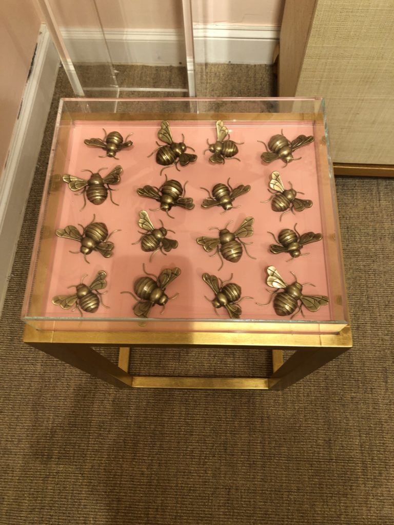 Gold based statement table featuring a case with a pink table top with golden bee sculptures within the case Lindsey Putzier Design Studio