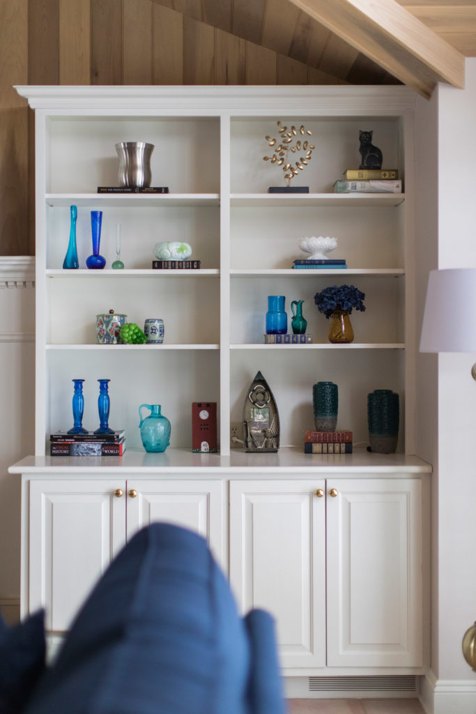 White built in cabinets filled with a colorful variety of decor accessories Lindsey Putzier Design Studio